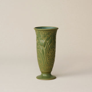 Green ceramic vase with carved flowers on a beige background.