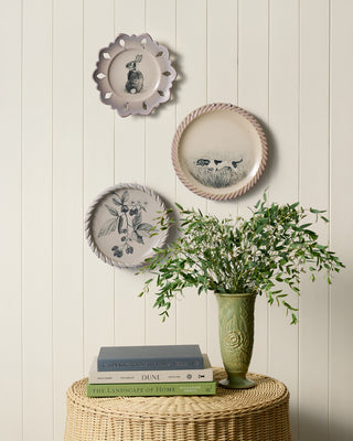 Decorative plates with animal illustrations on a white wall, accompanied by a vase with greenery and books.